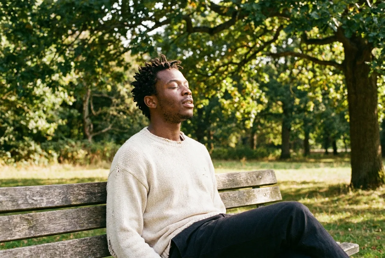 A young man on a park bench with his eyes closed, taking a slow, calm breath